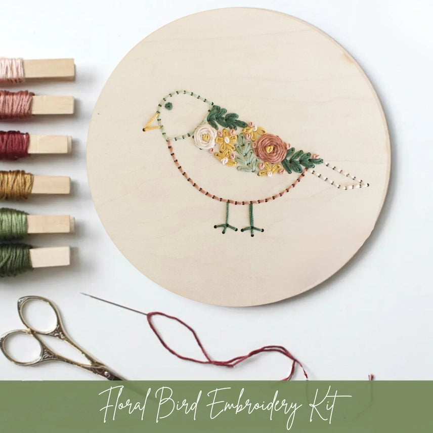 Embroidery hoop with floral bird design, embroidery threads, and scissors on a white background.