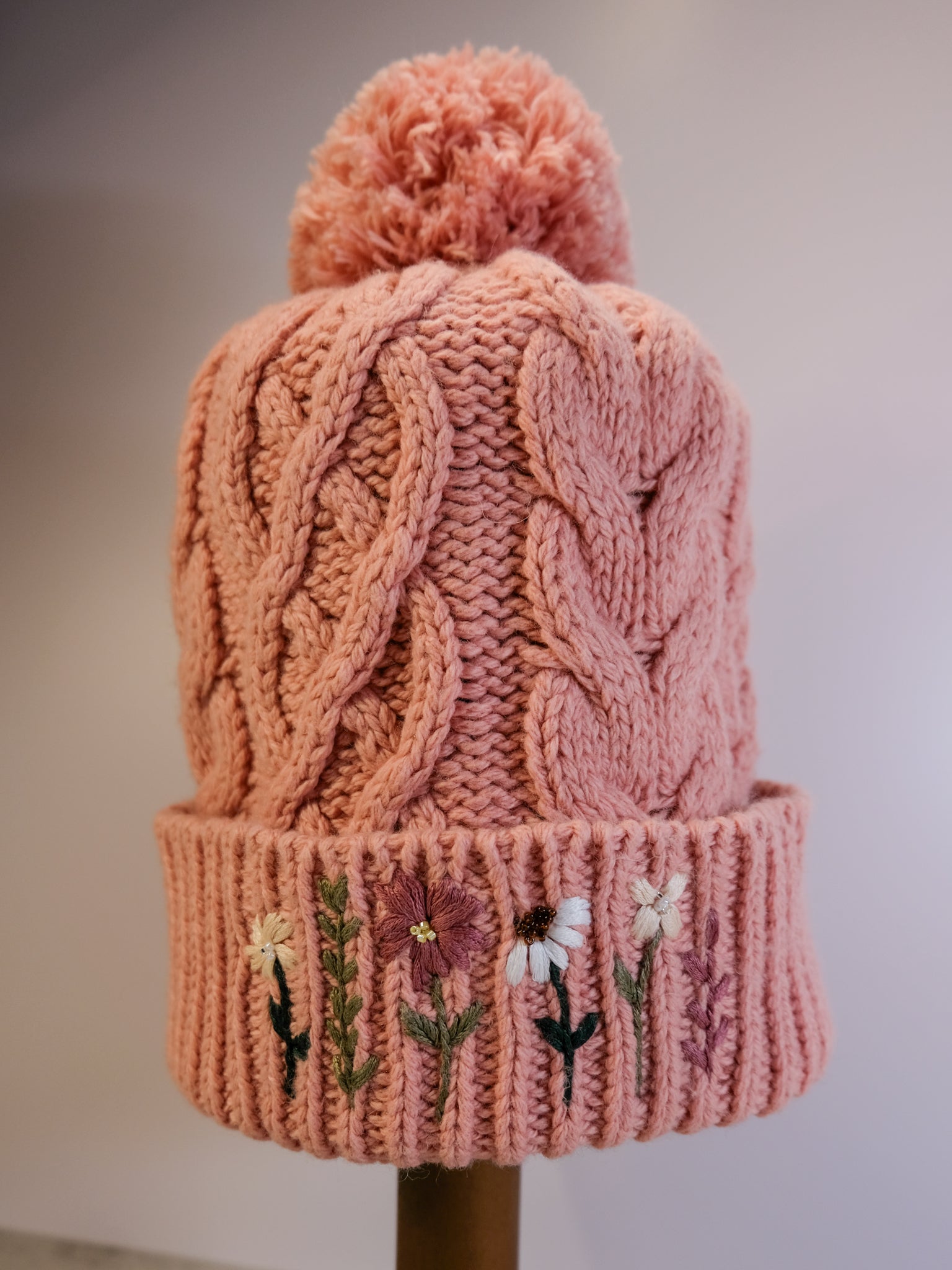 Pink knitted beanie with embroidered flowers on a neutral background
