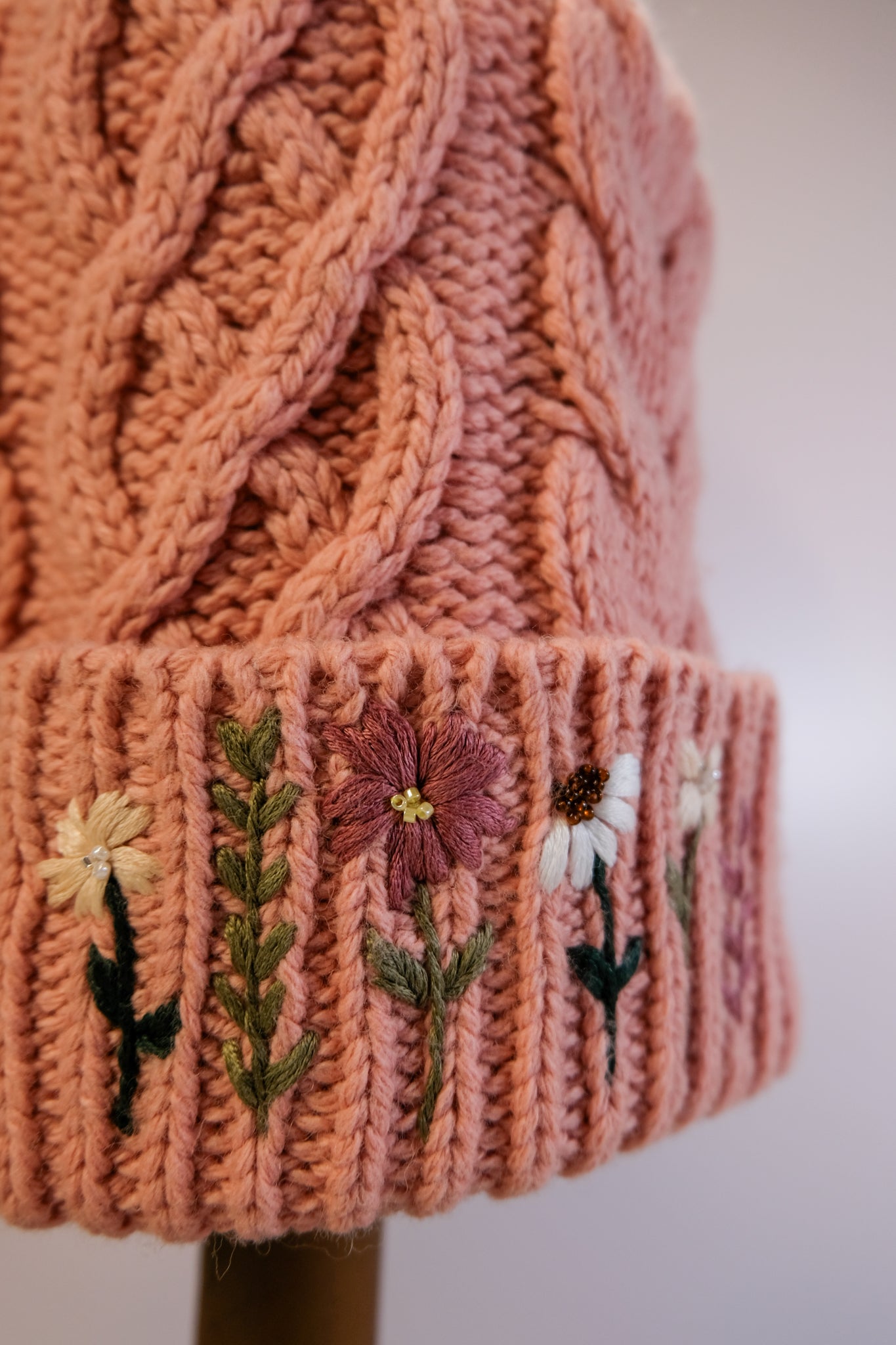 Pink knitted beanie with floral embroidery on a white background