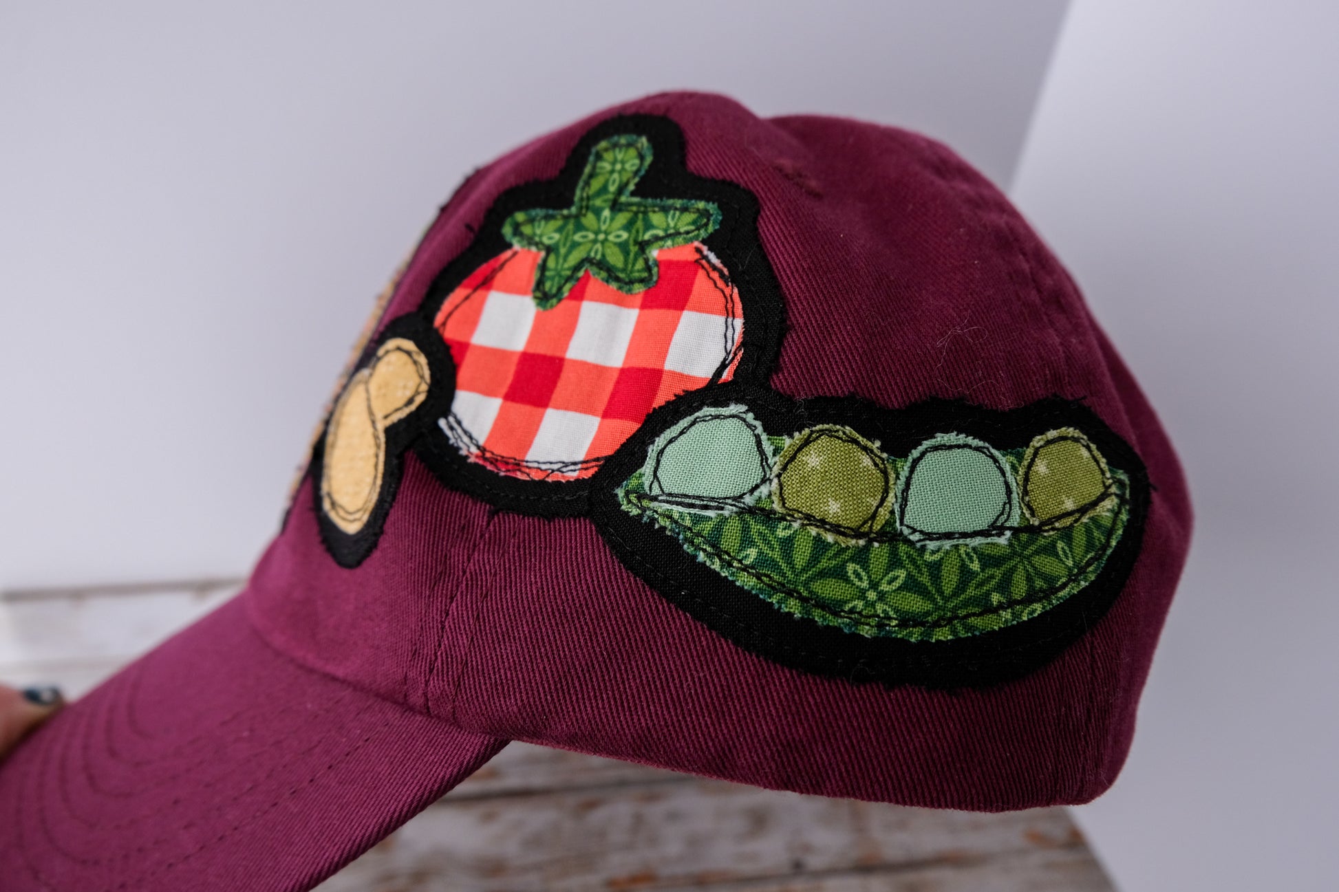 Maroon cap with tomato, mushrooms, and pea patch on a white background
