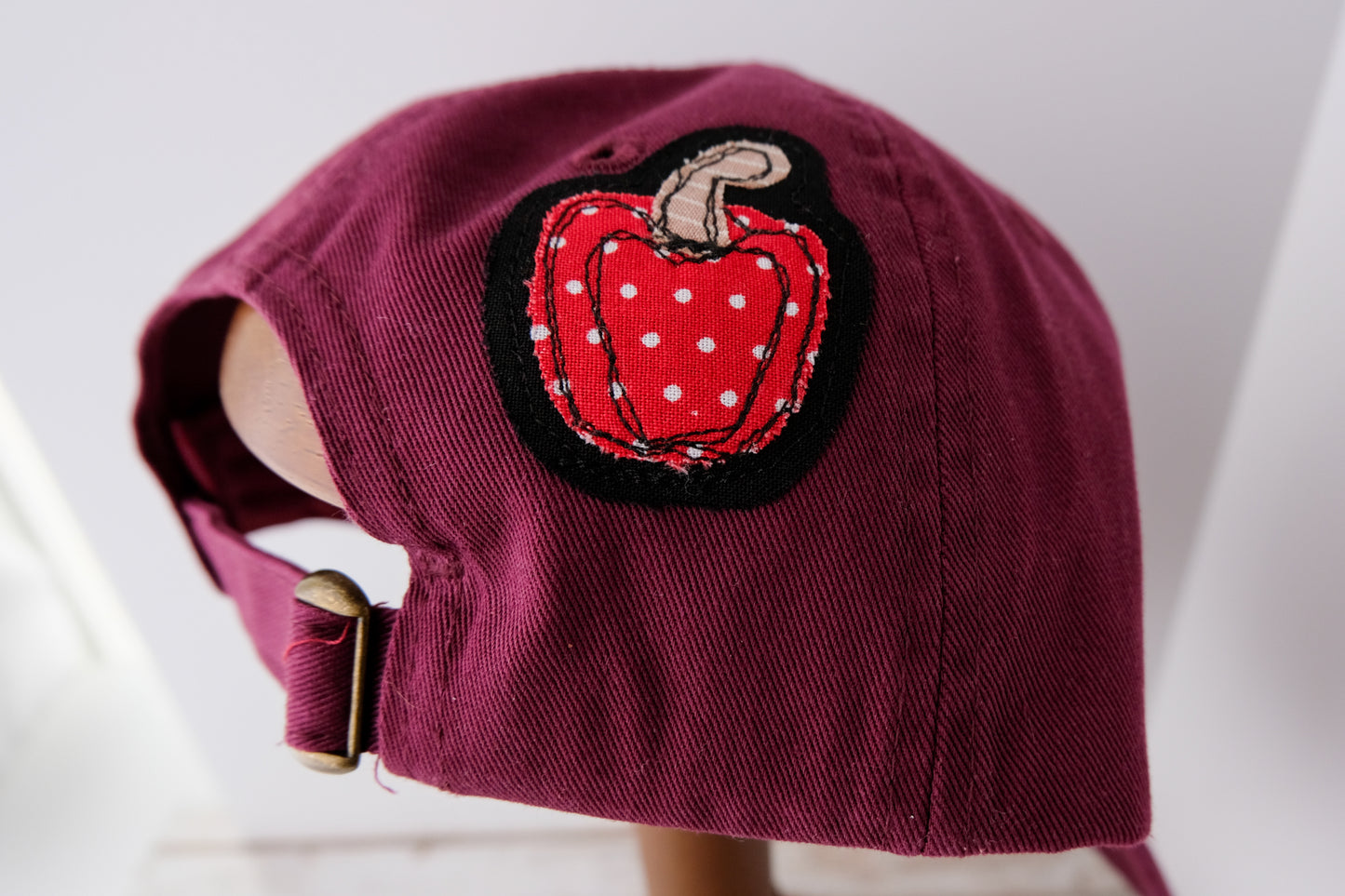 Maroon cap with a red polka dot bell pepper patch on a white background
