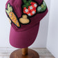 Maroon cap with vegetable patches on a wooden stand against a white wall.