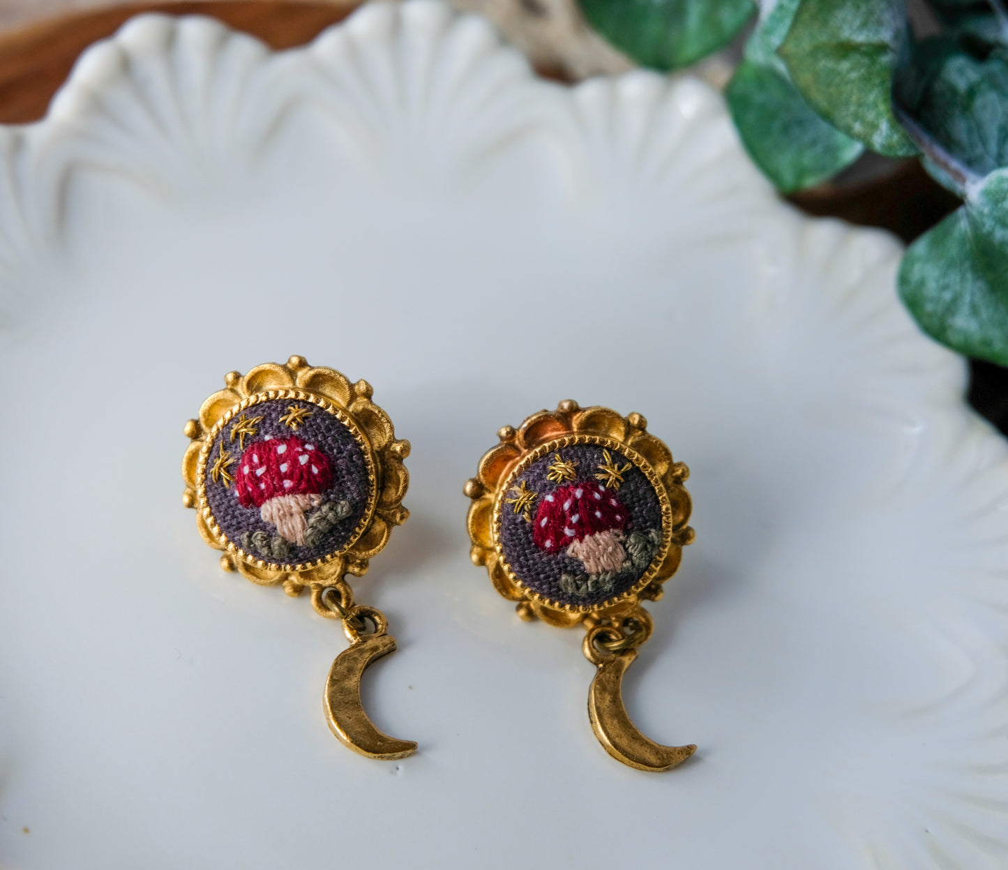 Pair of earrings with intricate embroidered mushroom design on a white plate