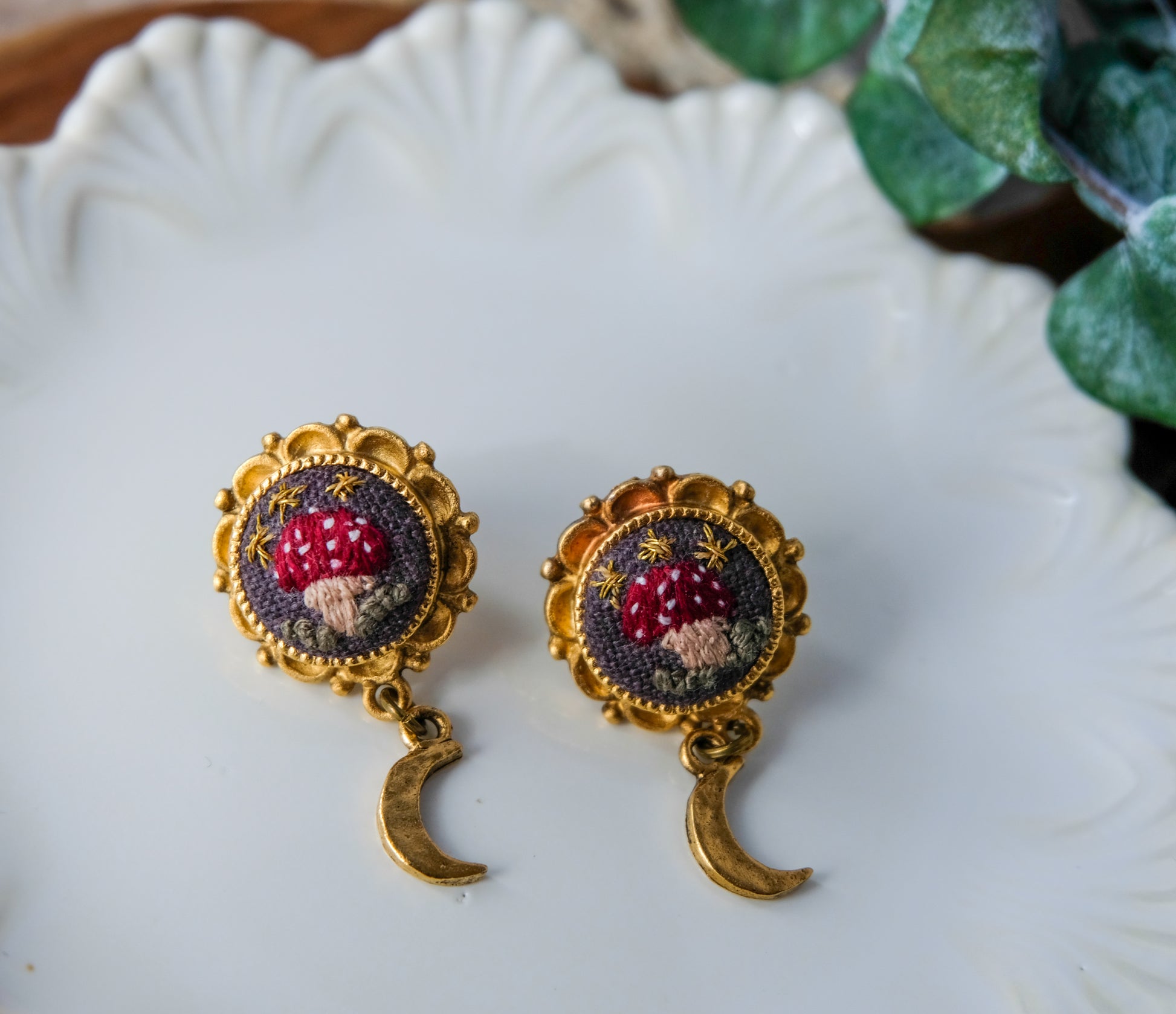 Pair of earrings with intricate embroidered mushroom design on a white plate