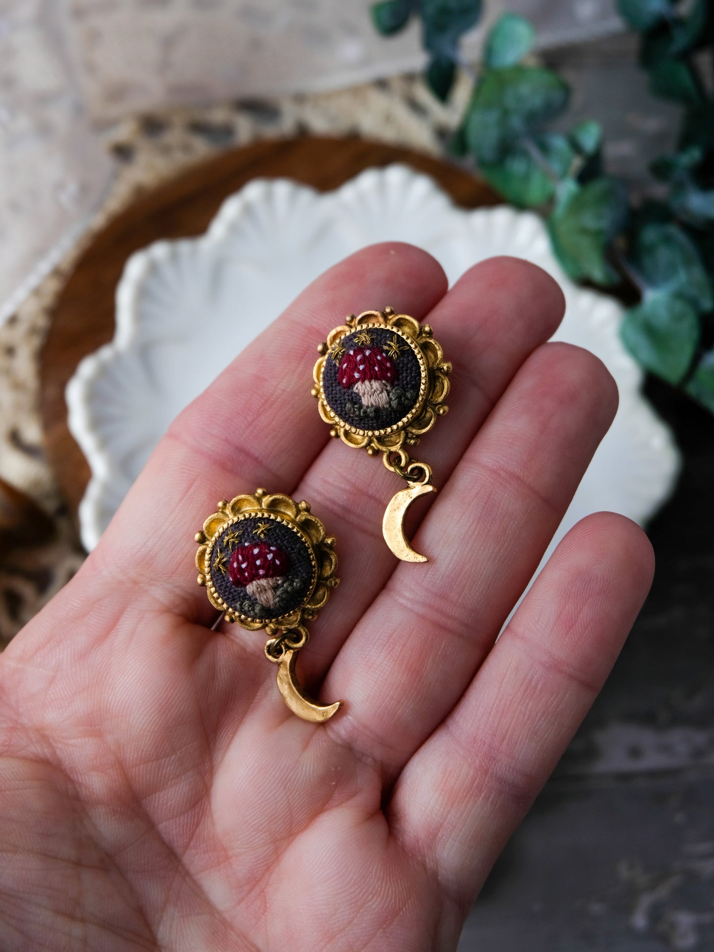 Gold earrings with red mushrooms held in a hand against a blurred background