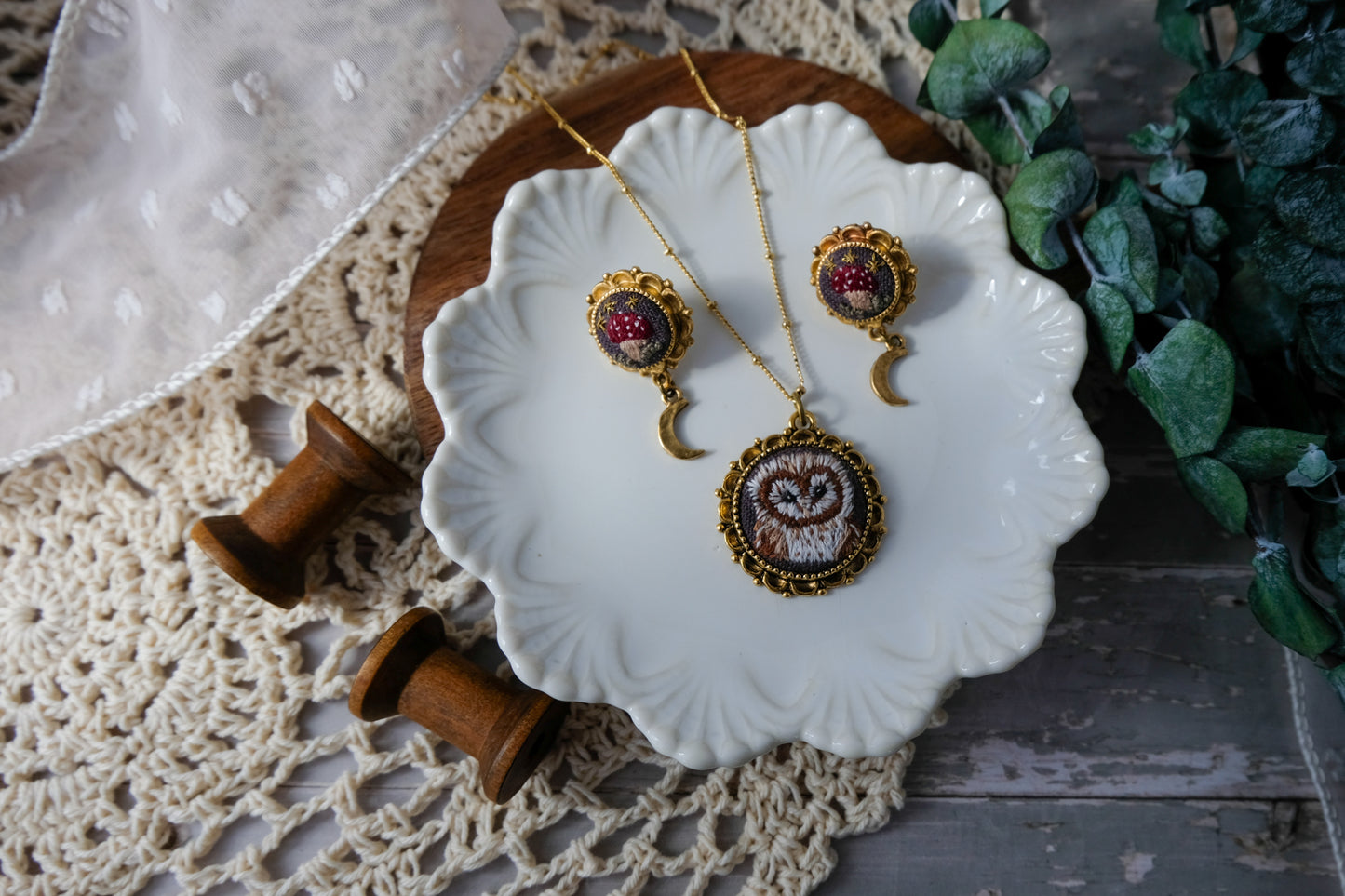 Decorative jewelry set on a white dish with a wooden surface and greenery in the background