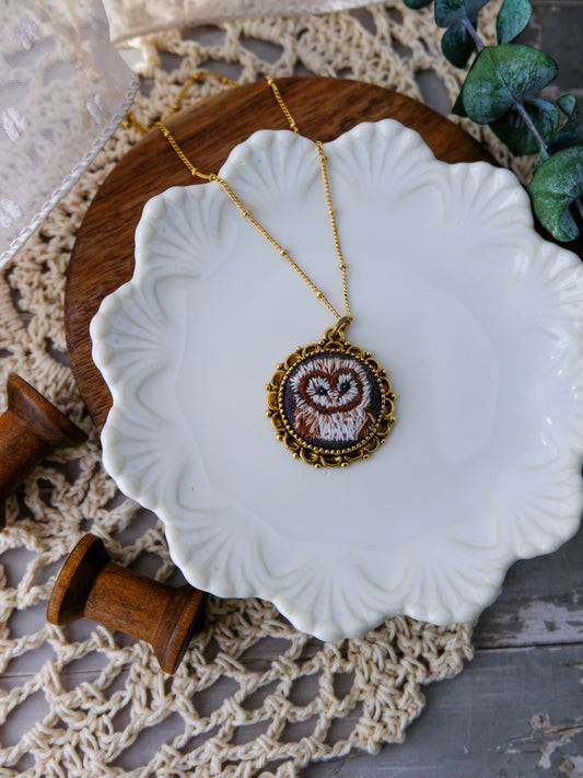 Necklace with an embroidered pendant on a white dish, wooden stand, and lace background