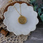 Gold necklace on a white ceramic dish with wooden spools and greenery in the background