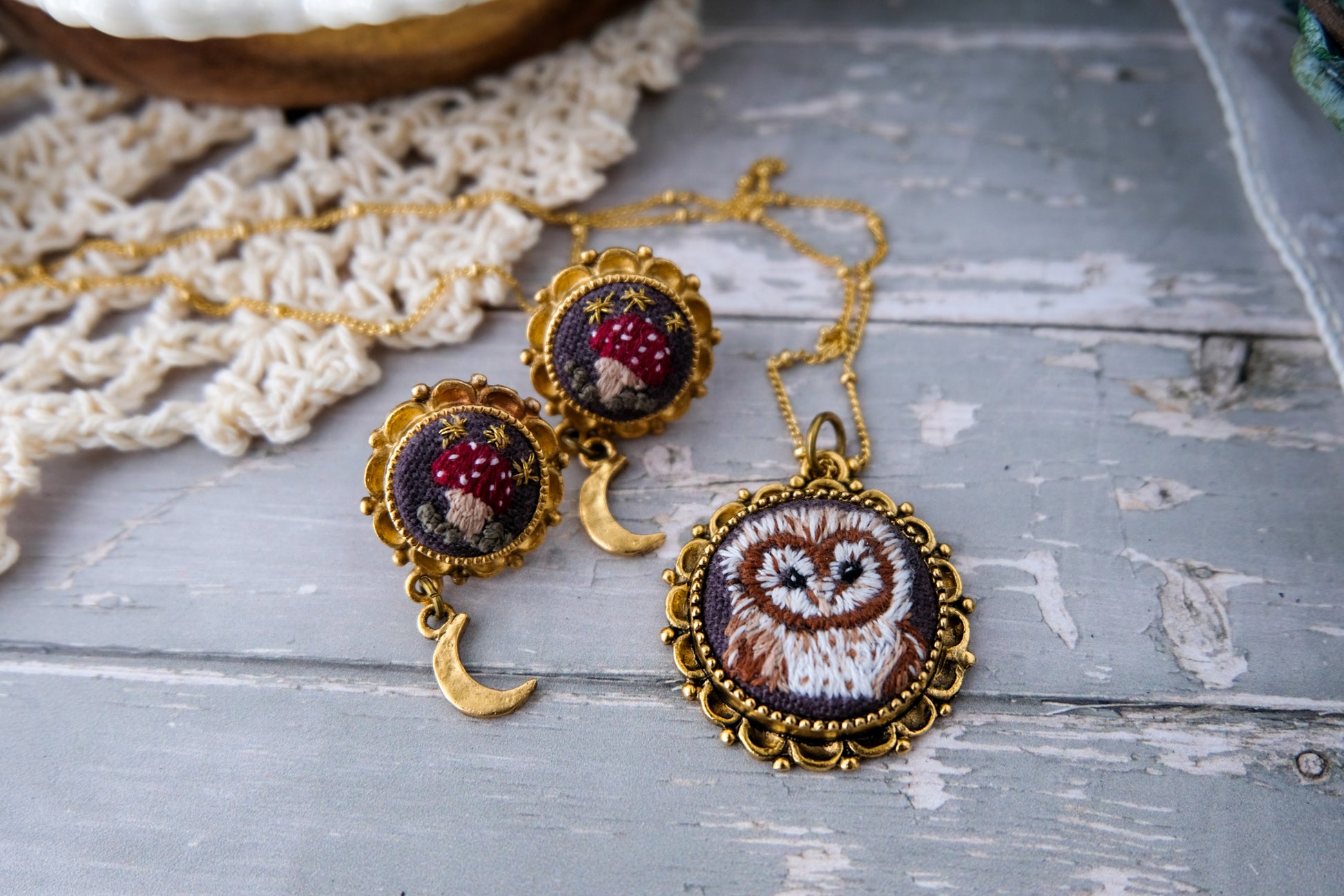 Jewelry set with owl pendant and red mushroom earrings on a textured wooden surface