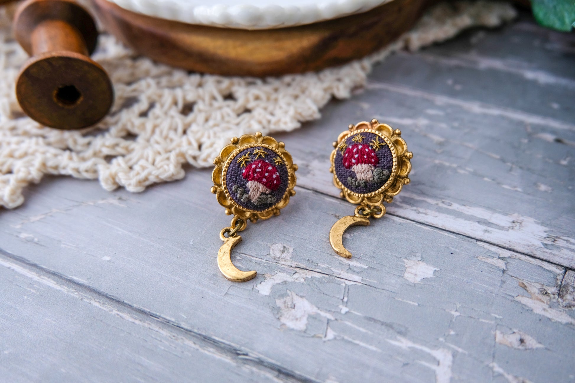 Pair of embroidered earrings on a textured surface with a wooden spool in the background.