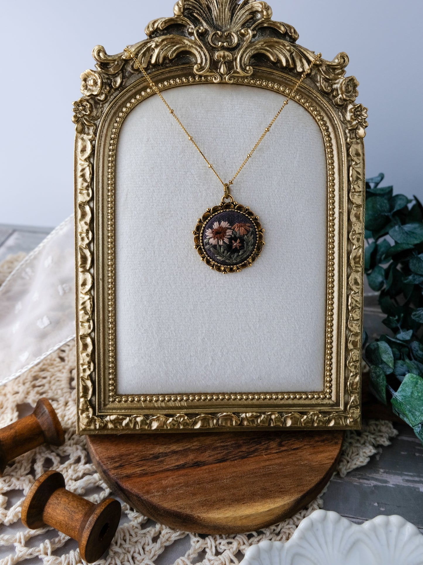 Decorative gold frame with a necklace featuring a pendant on a textured surface.