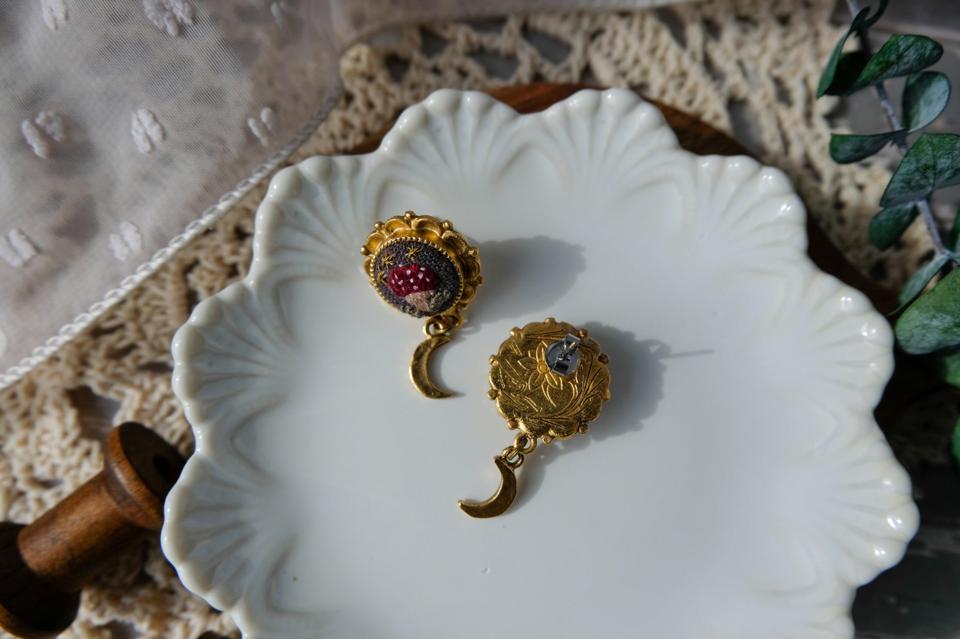 Gold earrings with red mushrooms on a decorative white dish.