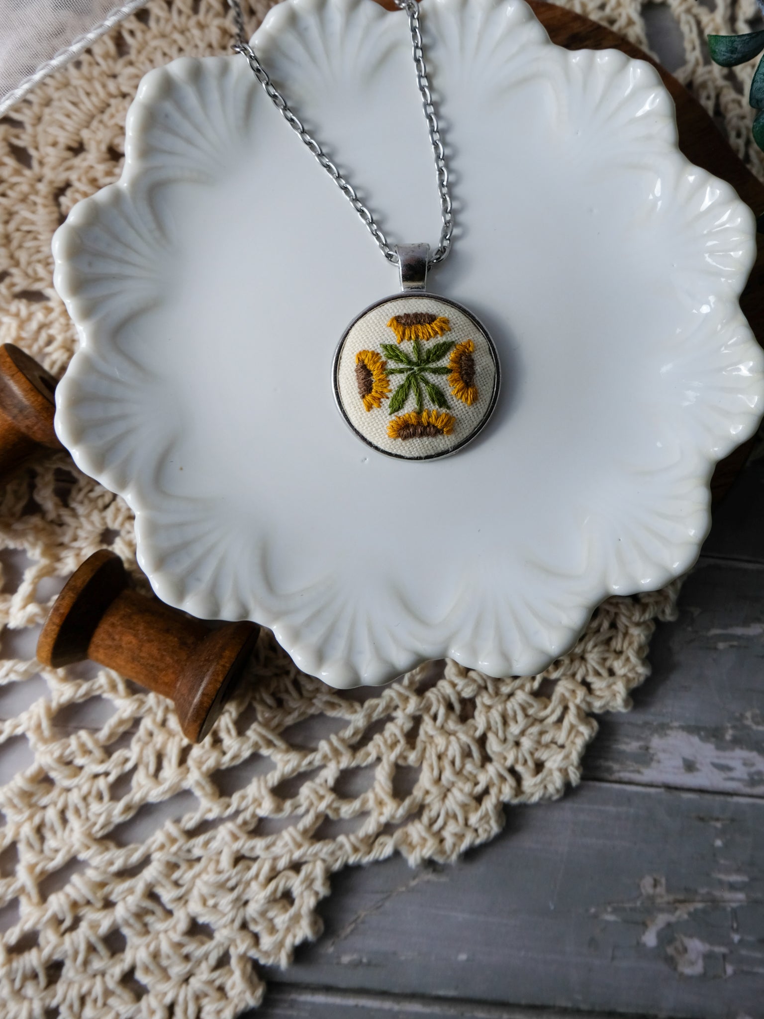 Necklace with a floral pendant on a white dish with a wooden handle, on a textured surface.