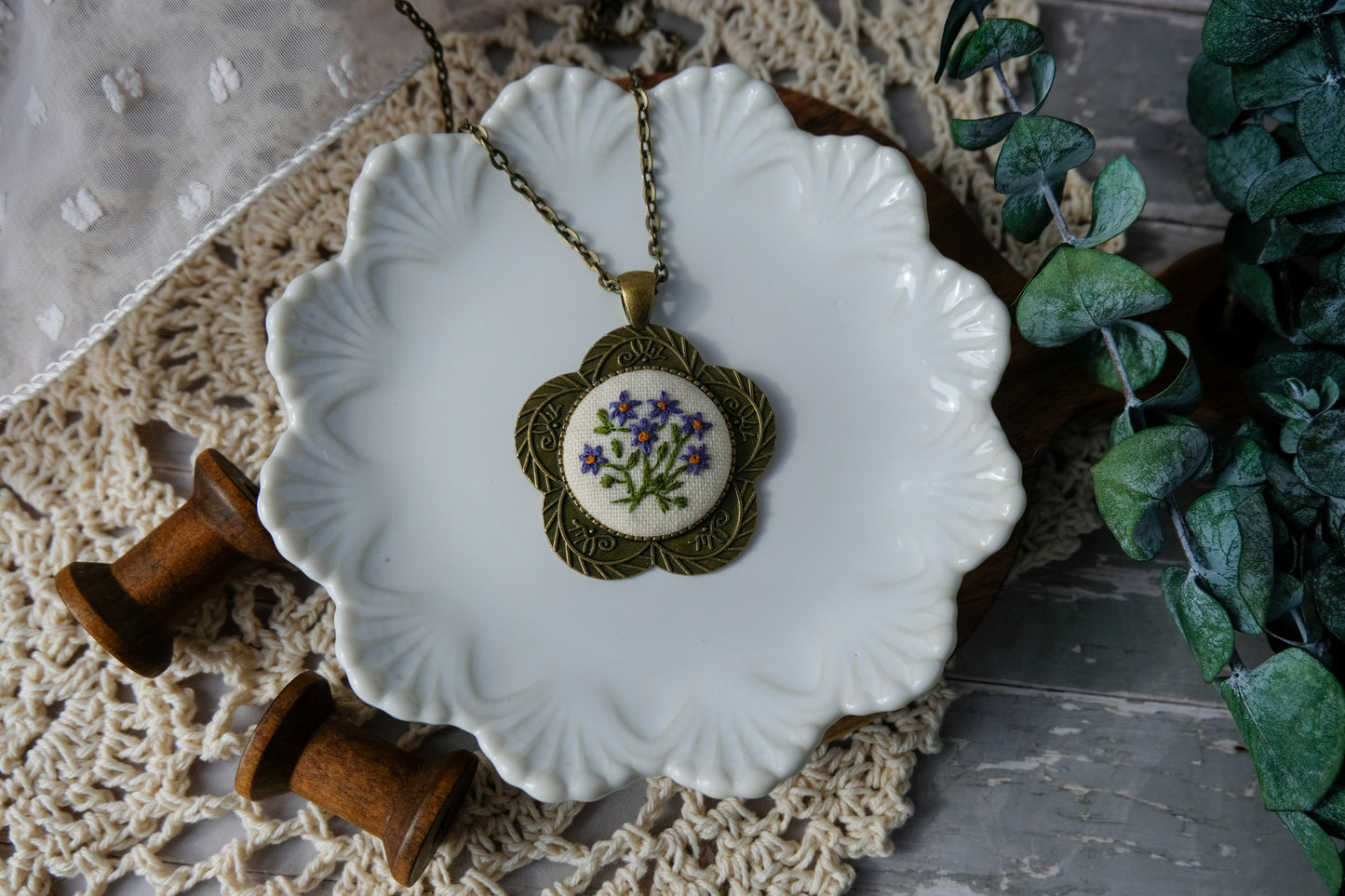 Necklace with floral pendant on a decorative plate with greenery in the background