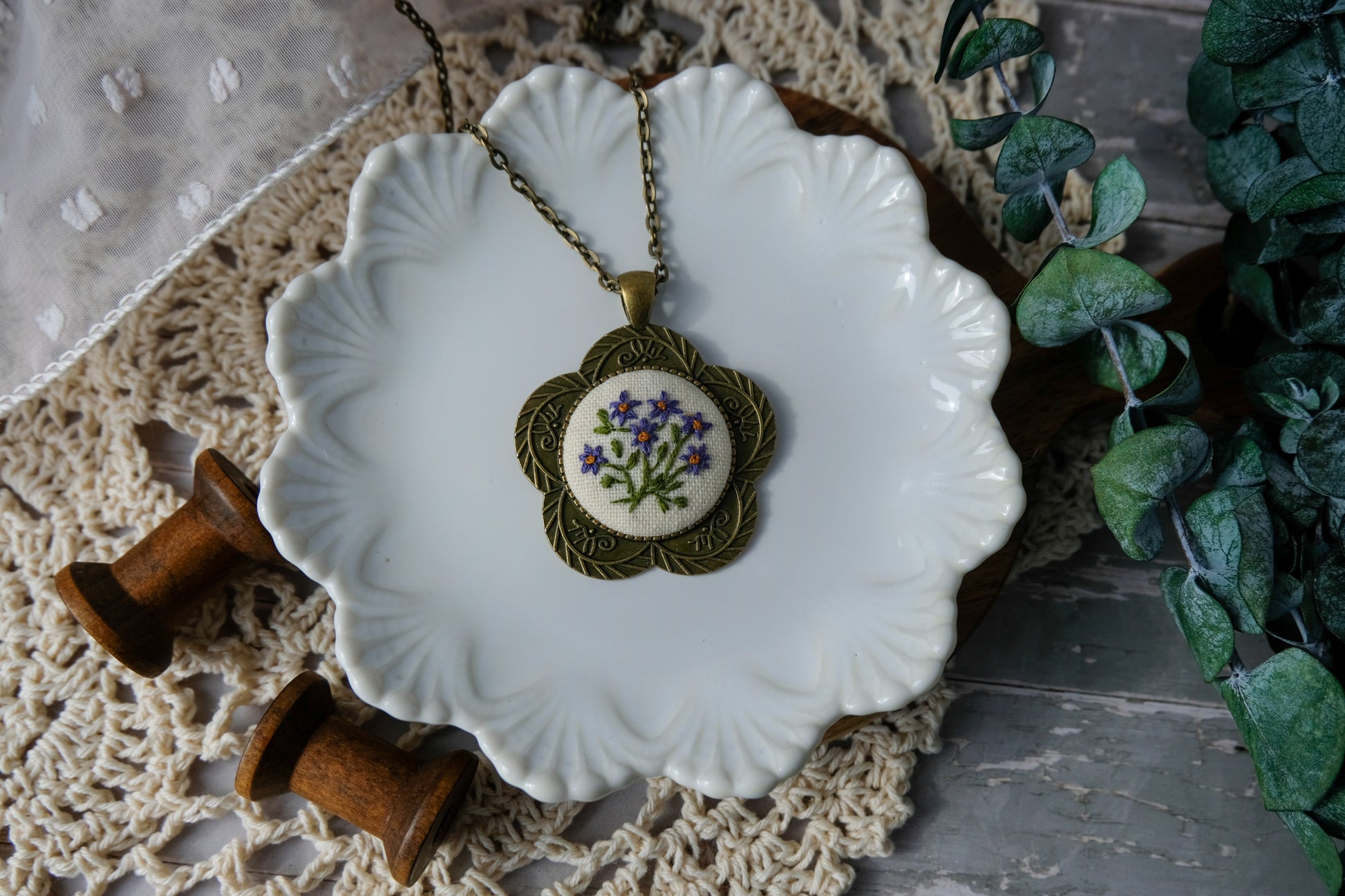Necklace with floral pendant on a decorative plate with greenery in the background