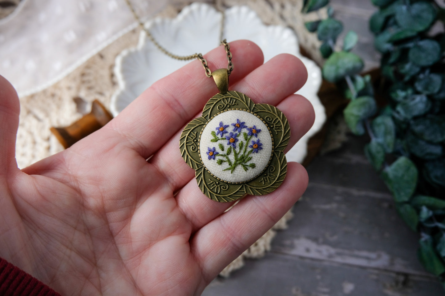 Hand holding a decorative pendant with floral design against a blurred background