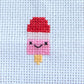 Cross-stitched design of a pink ice cream with a red top on a light blue fabric background.