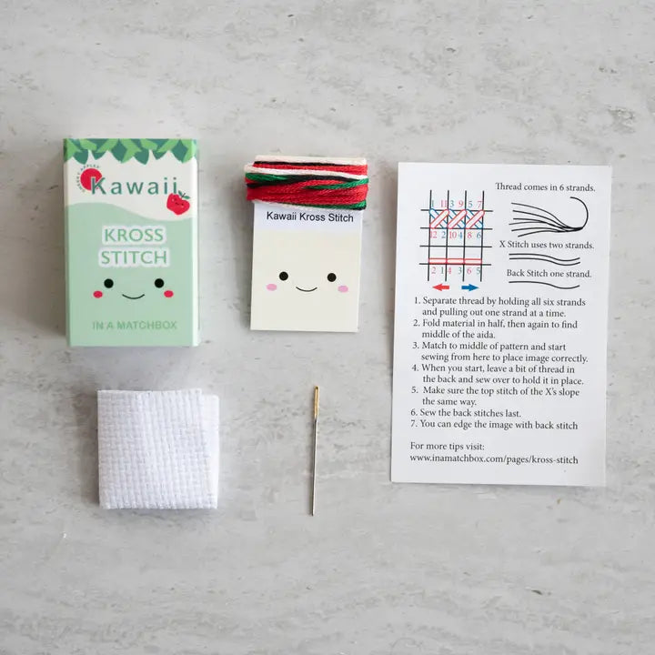 Kawaii-themed cross-stitch kit with a needle and pattern card on a gray surface